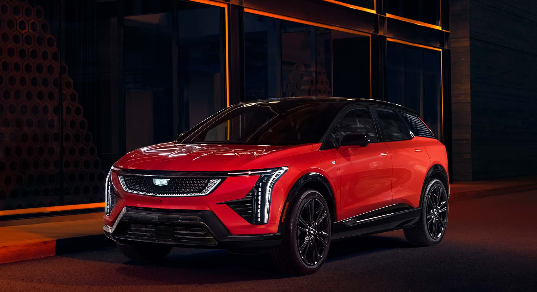 Red Cadillac OPTIQ is parked in front of a building at night