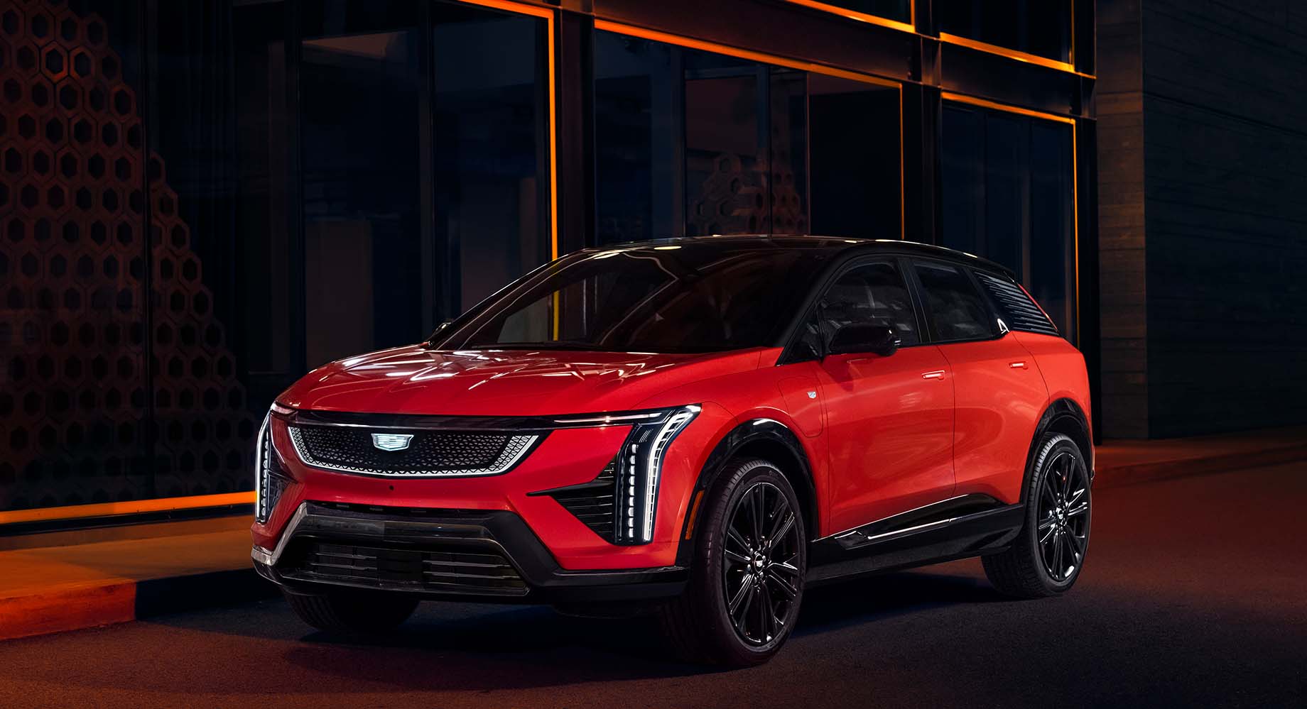 Red Cadillac OPTIQ is parked in front of a building at night