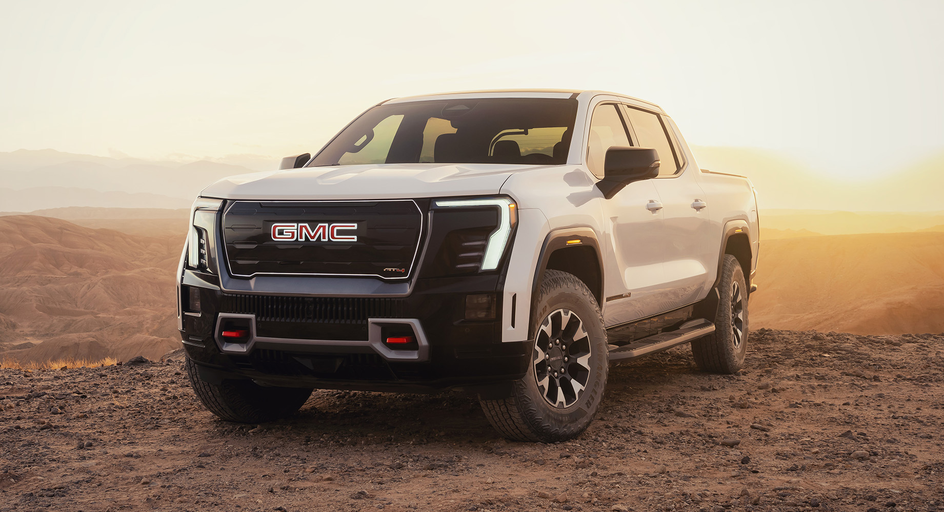A white GMC Sierra EV in a vast desert at sunset