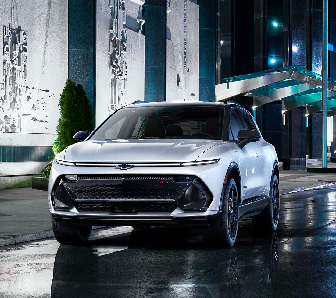 White Chevrolet Equinox EV is parked in front of a building at night