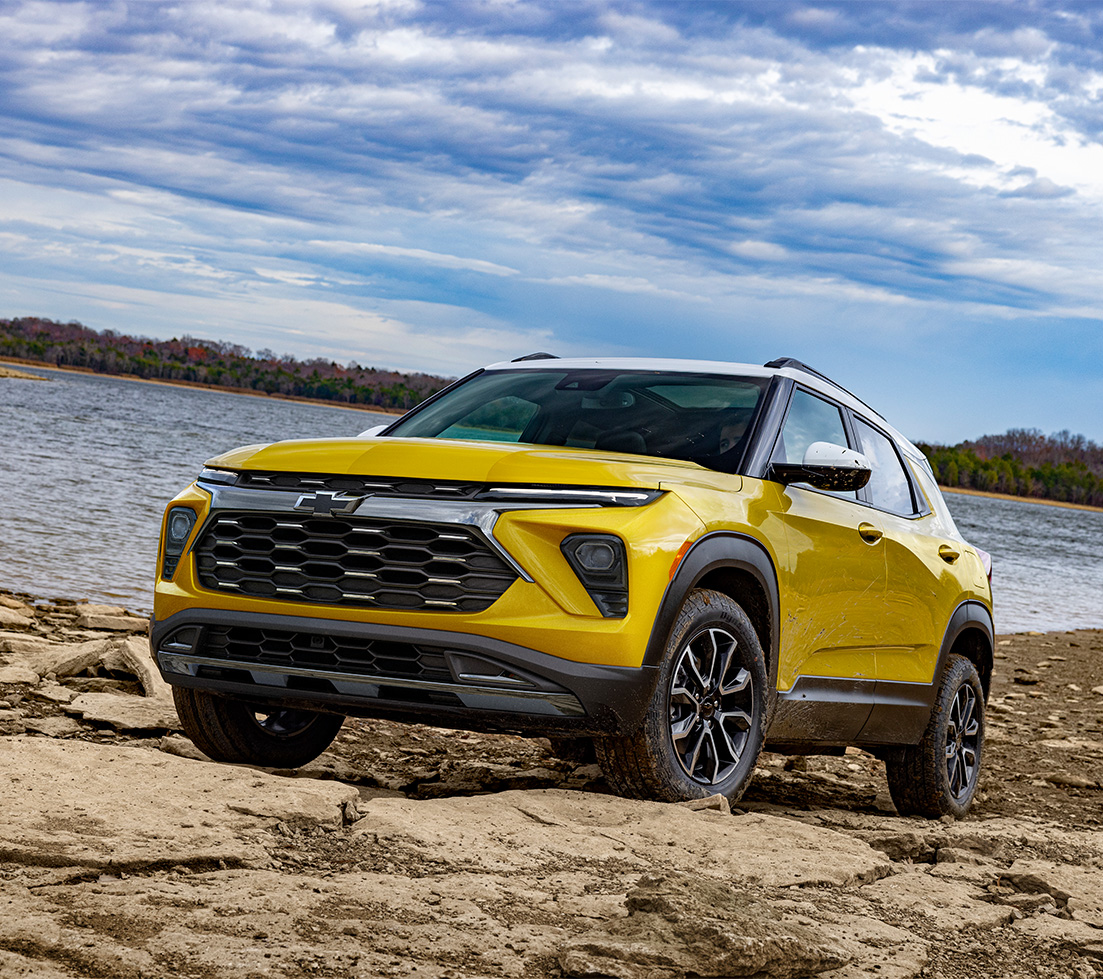 A yellow Chevrolet Trailblazer is parked on a rocky beach
