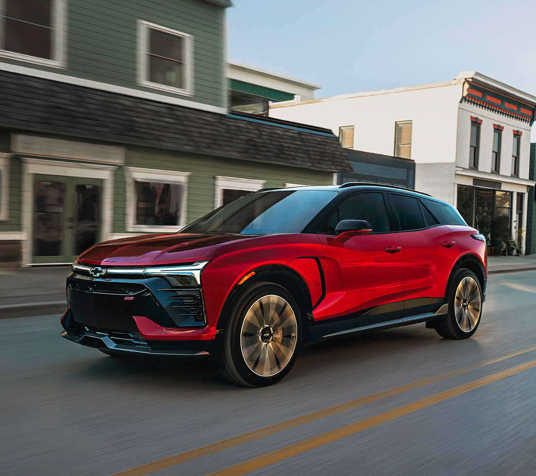 Red Chevy Blazer EV driving in front of a green building