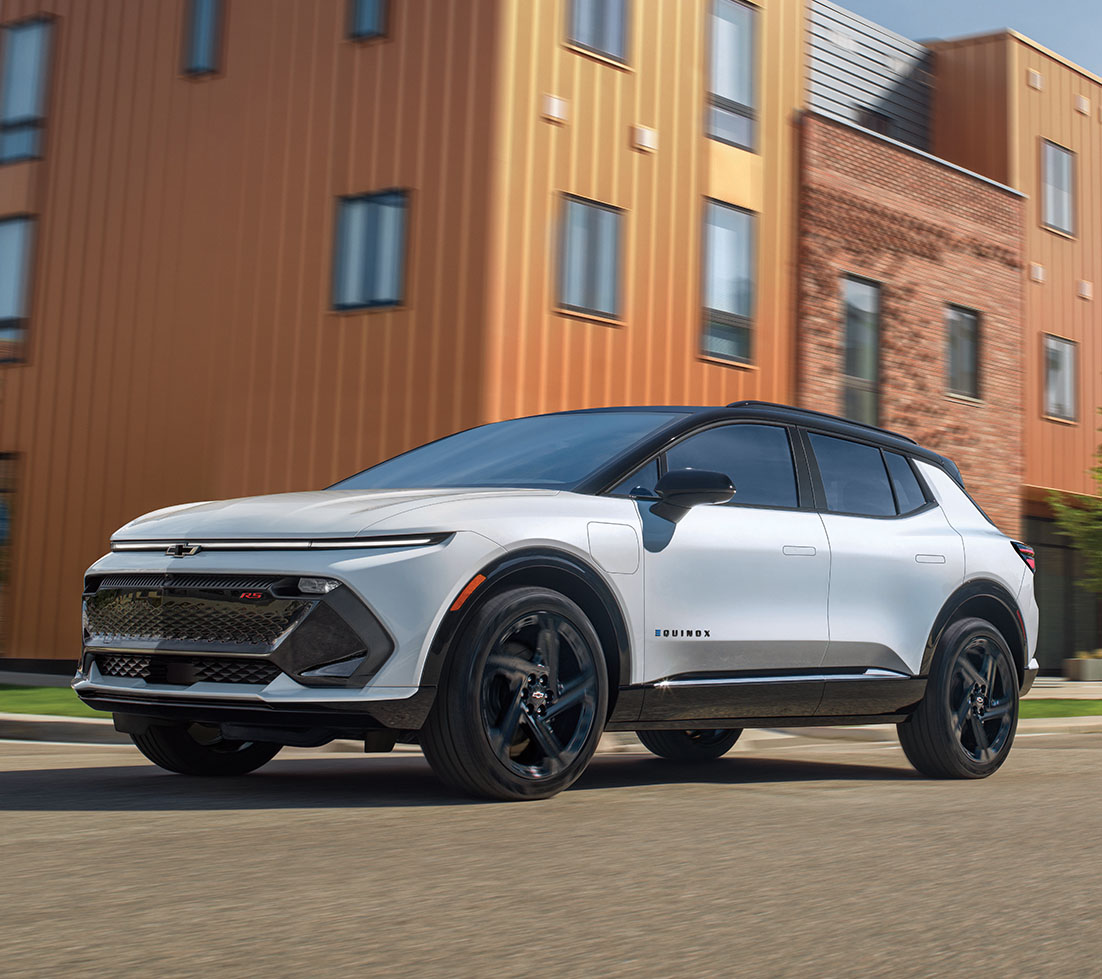 White Chevy Equinox EV driving in front of a brick building