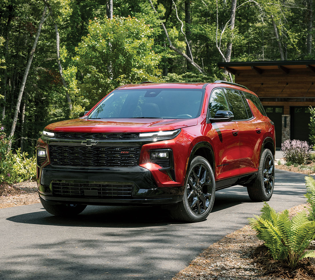 Un Chevrolet Traverse rouge garé dans l'allée d'un chalet en forêt