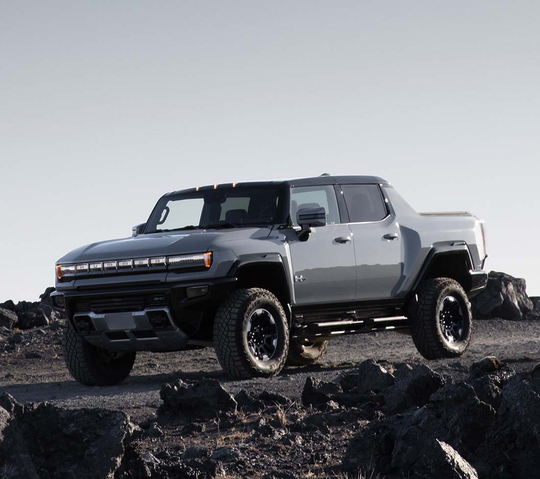 Gray GMC HUMMER EV SUT is driving down a dirt road surrounded by rocks