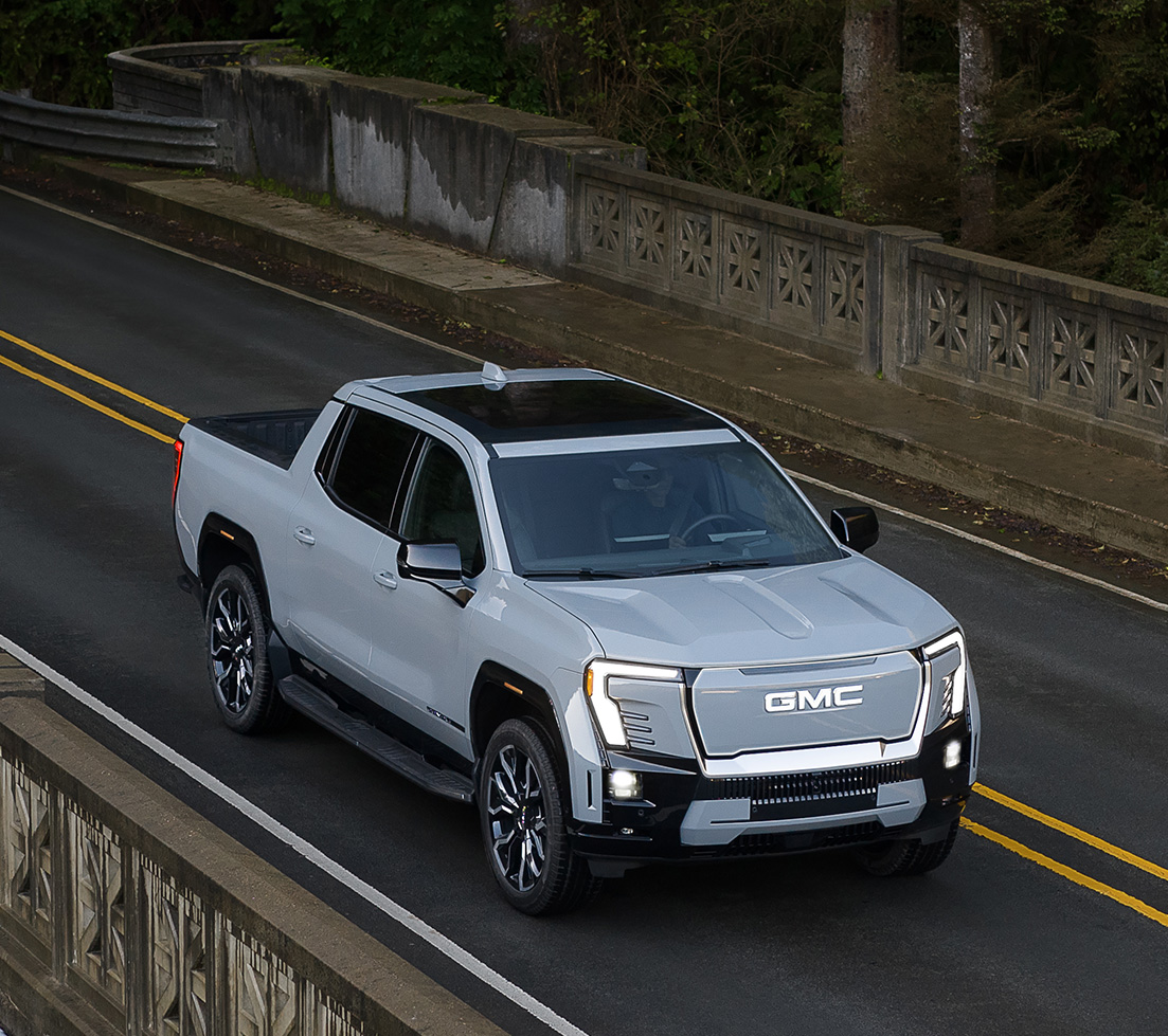 Gray GMC HUMMER EV SUT is driving down a dirt road surrounded by rocks