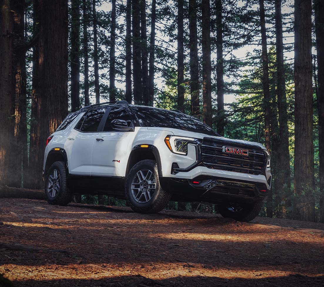 White GMC Terrain is driving down a dirt road in the woods