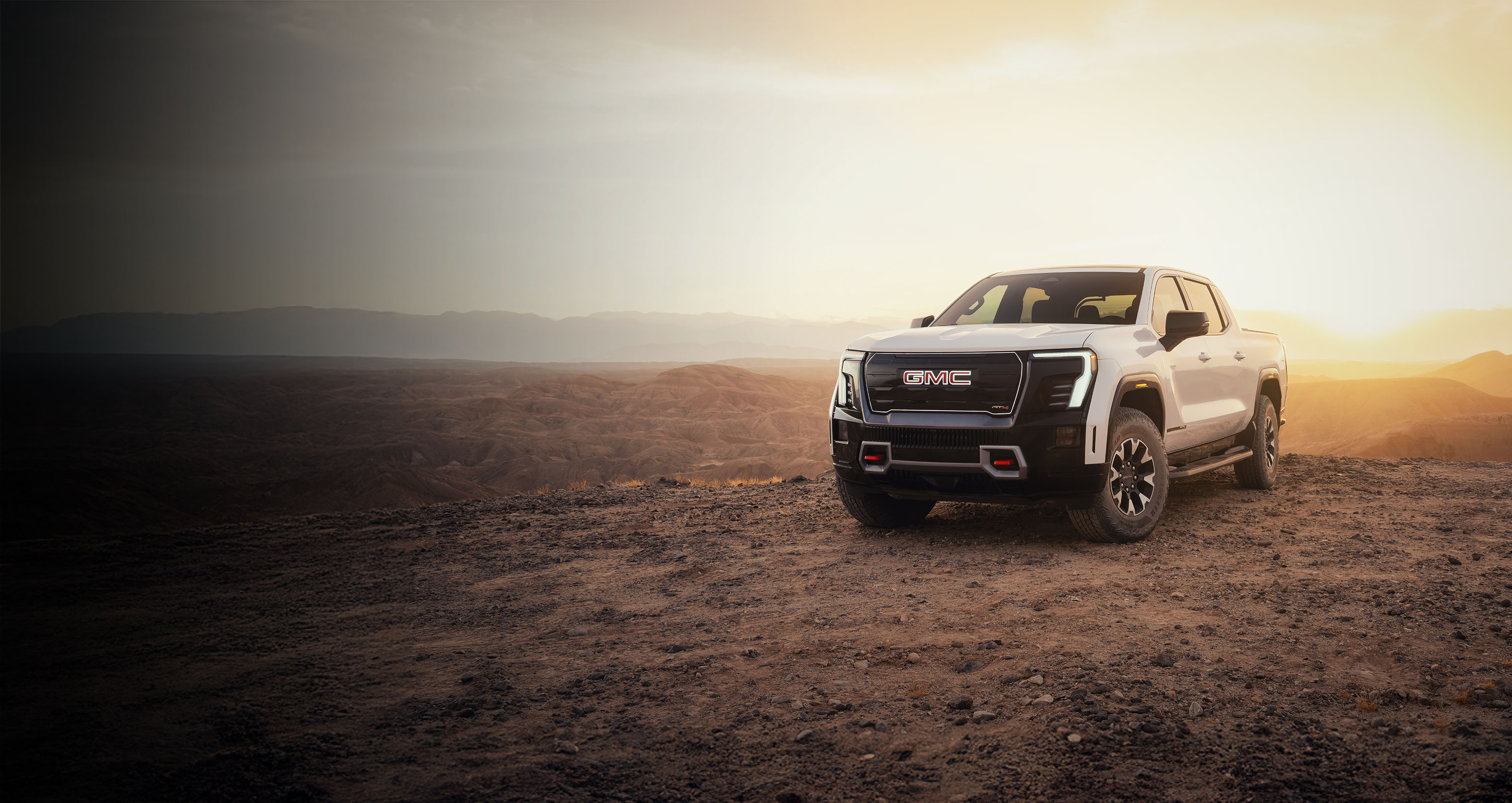 A white GMC Sierra EV in a vast desert at sunset