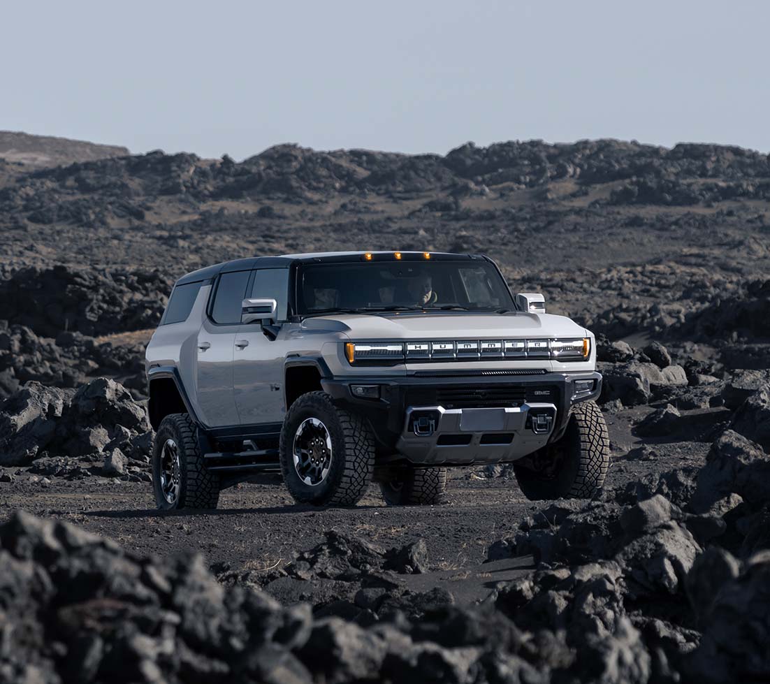 White GMC HUMMER EV SUV is parked in the middle of a rocky desert
