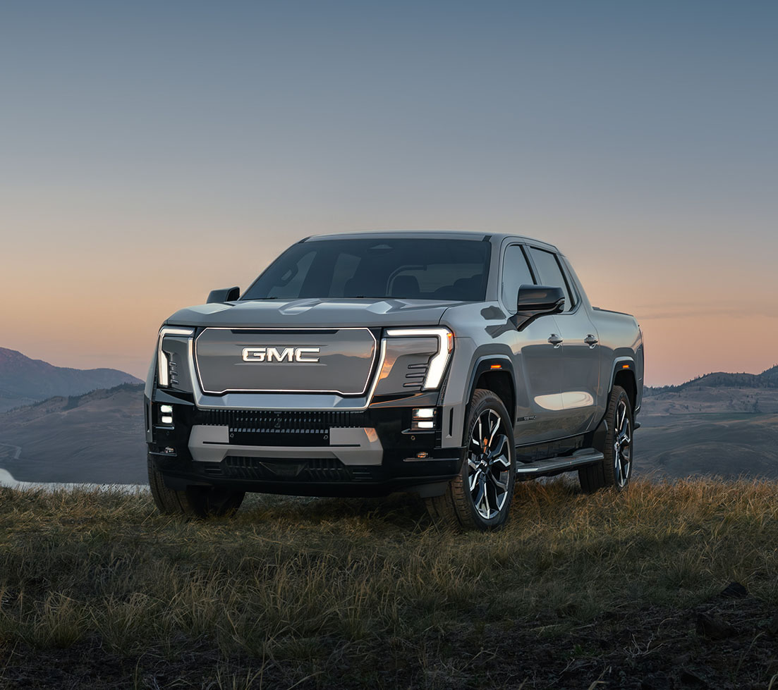 Gray GMC Sierra EV is parked on top of a grassy hill