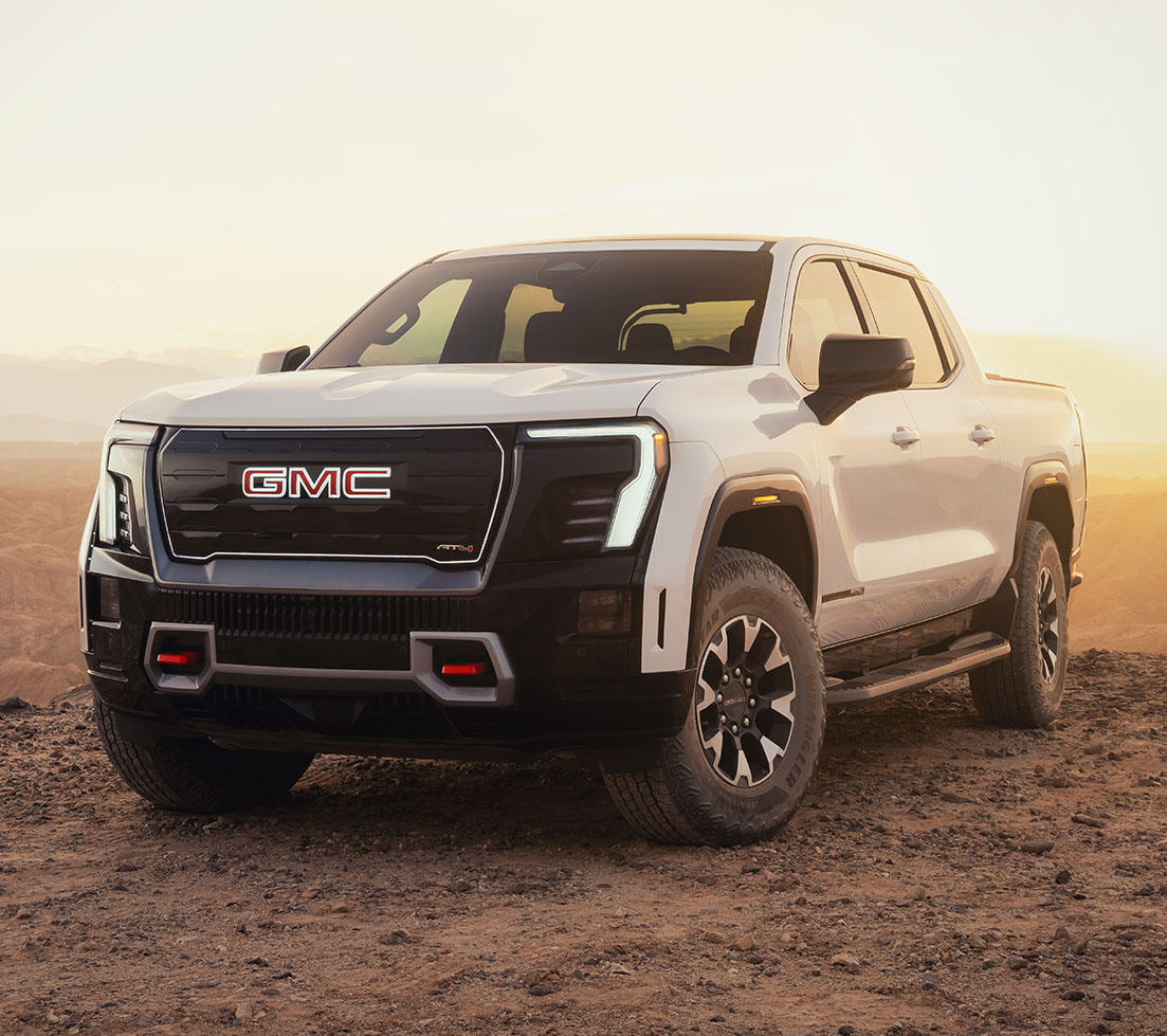 A white GMC Sierra EV in a vast desert at sunset